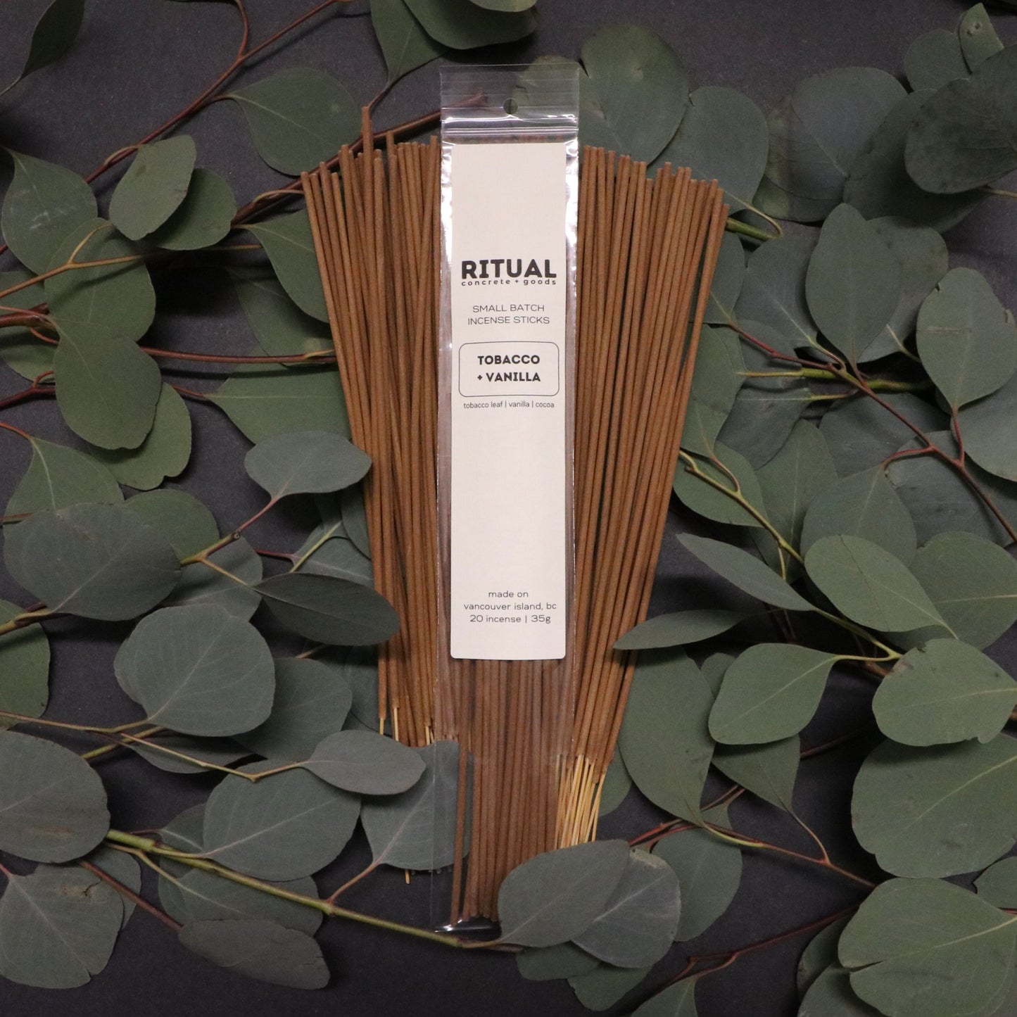 Pack of incense sticks with packaging on a dark surface with green leaves