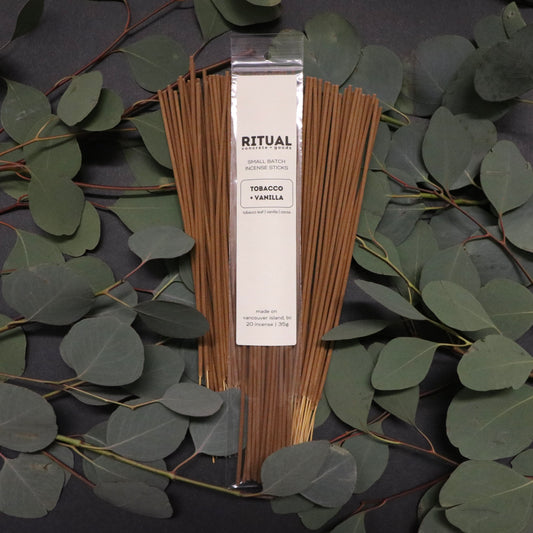 Pack of incense sticks with packaging on a dark surface with green leaves